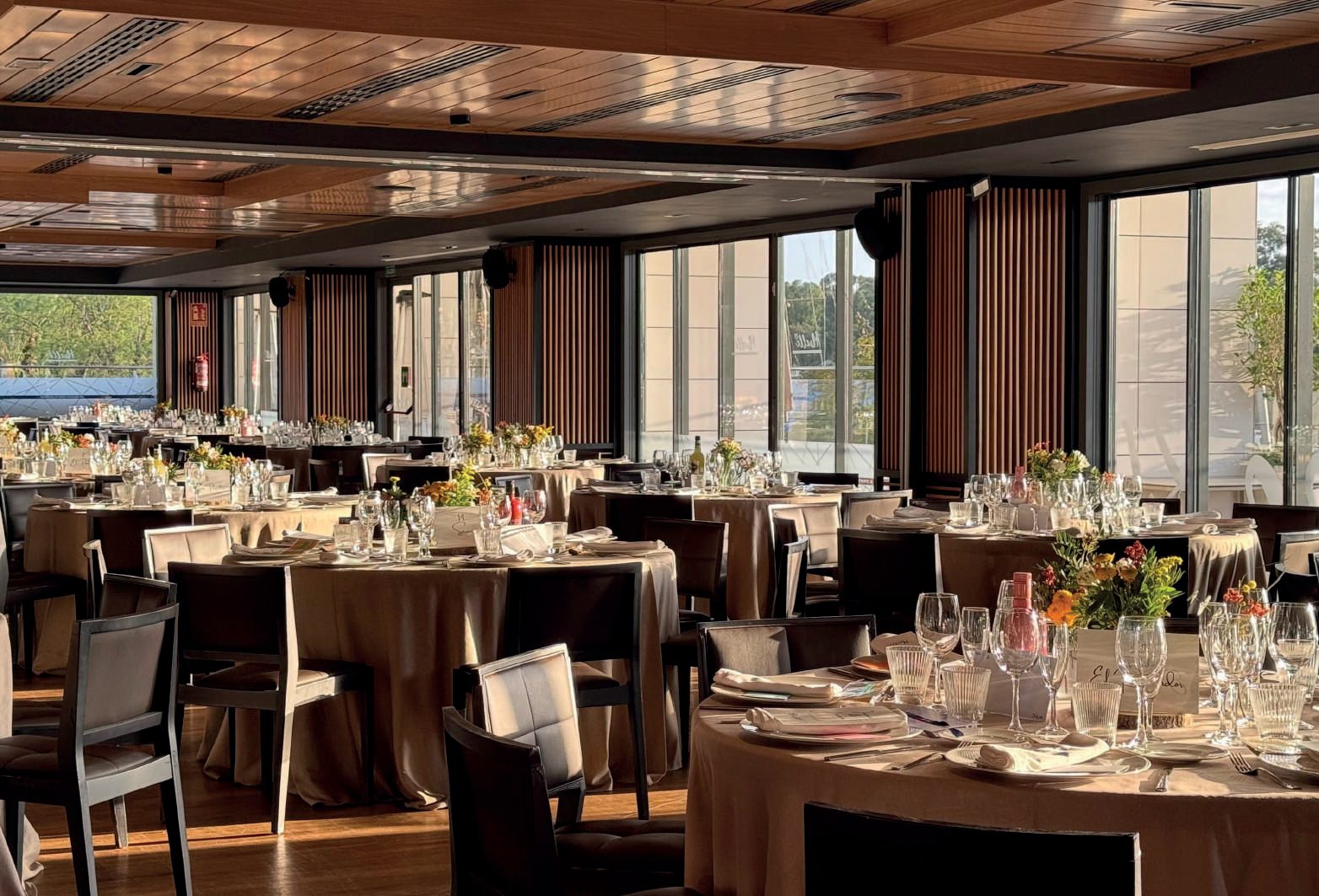 Salón con techo de madera y mesas preparadas junto a los ventanales
