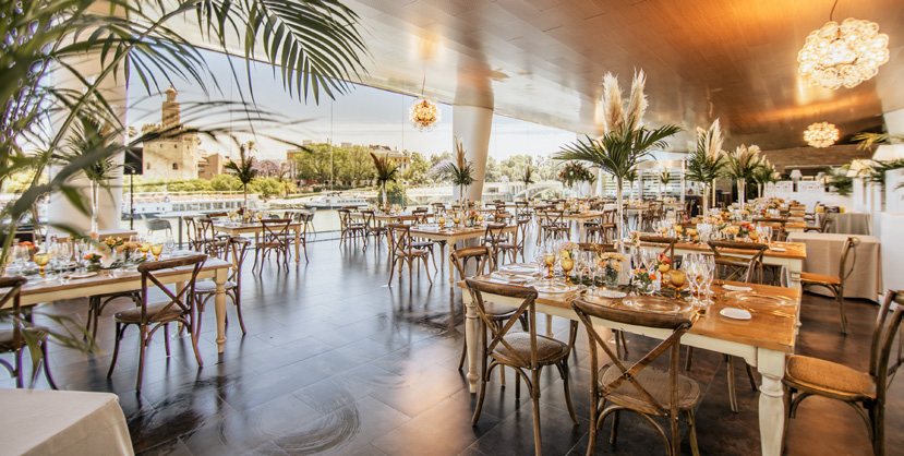 Salón acristalado con mesas preparadas y vistas al río